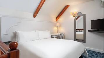 A hotel room with a large bed, a desk, a chair, a TV, and a mirror.