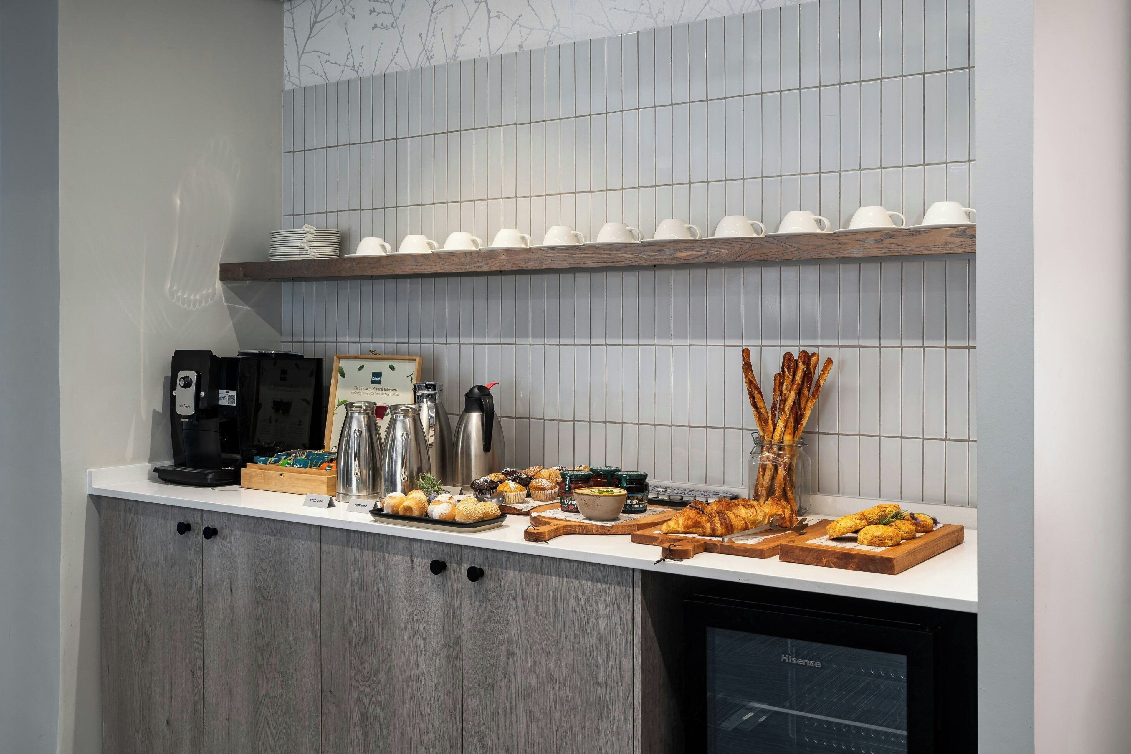 A kitchen counter with various food items, coffee makers, and a dishwasher.