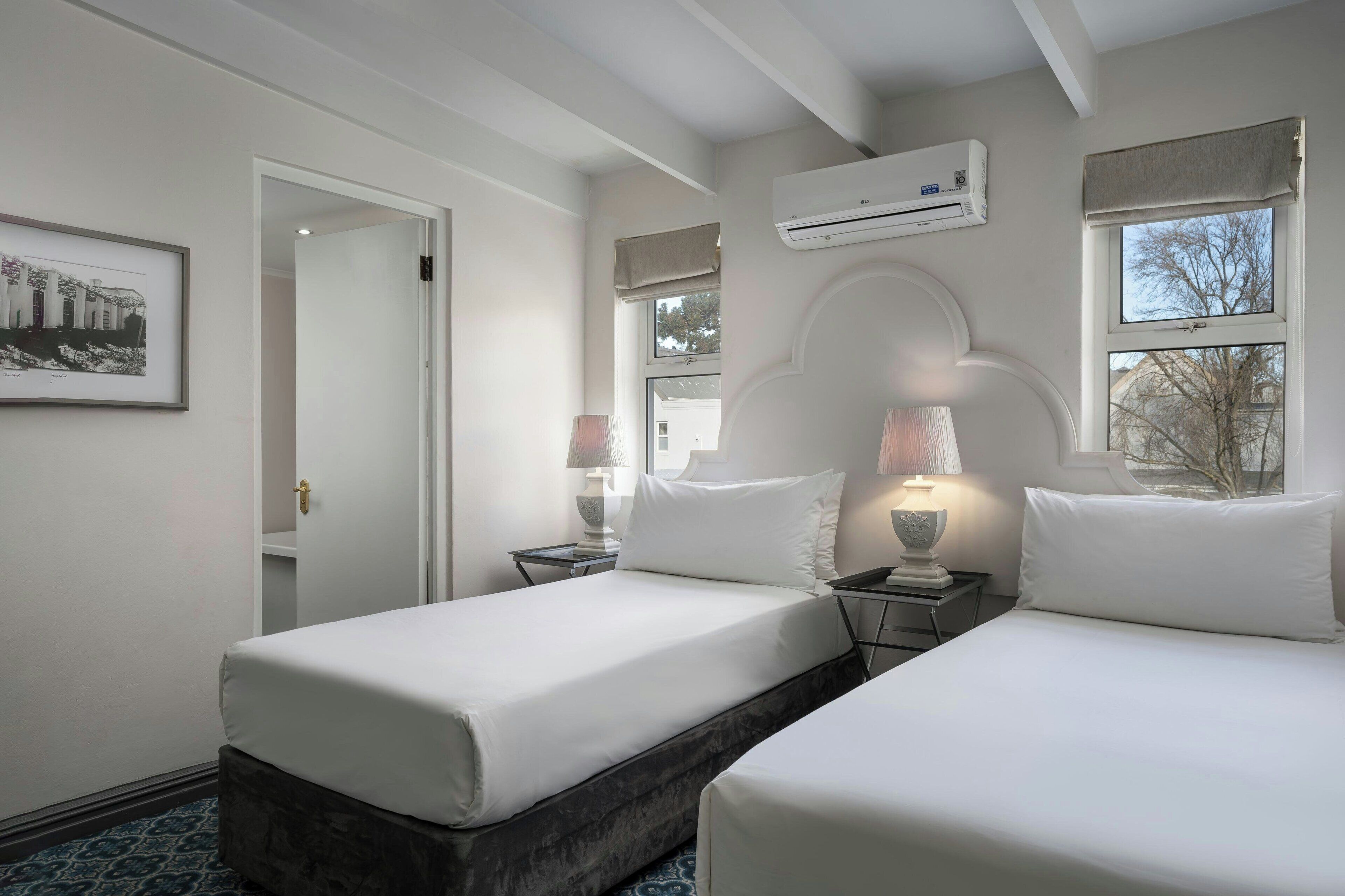 A hotel room with two beds, a door leading to another room, an air conditioning unit, and a window with a view.