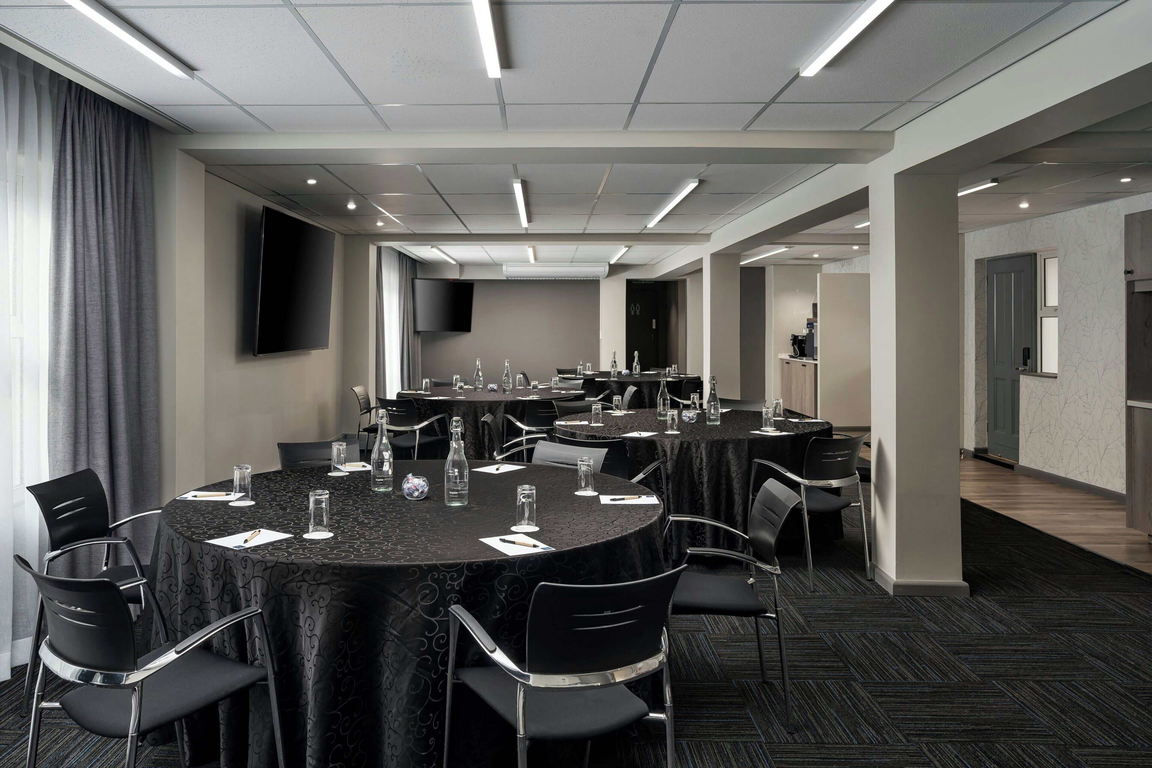 A conference room with round tables, chairs, and a flat-screen TV.