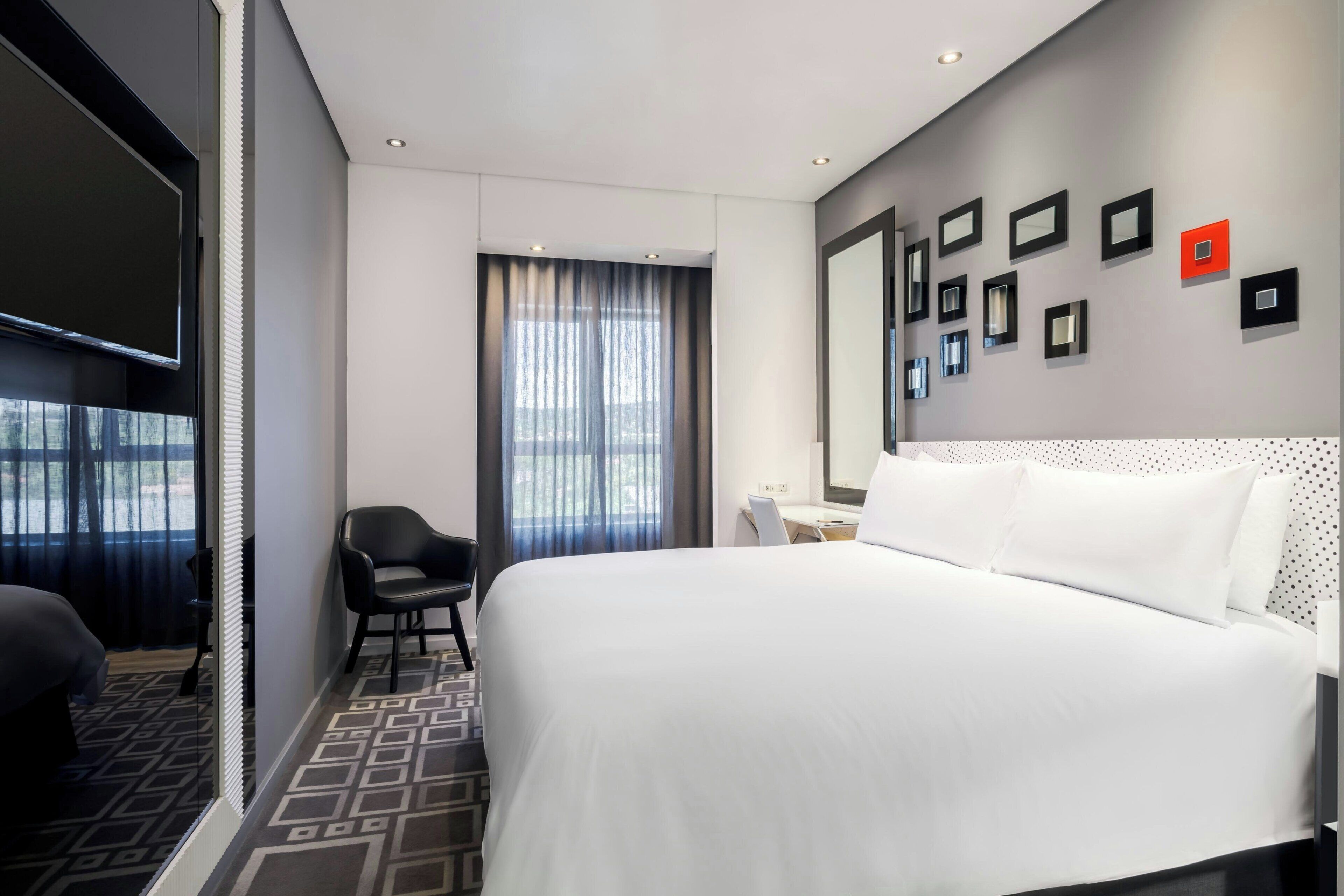 A hotel room with a large bed, a desk, a chair, a TV, and a window with curtains.
