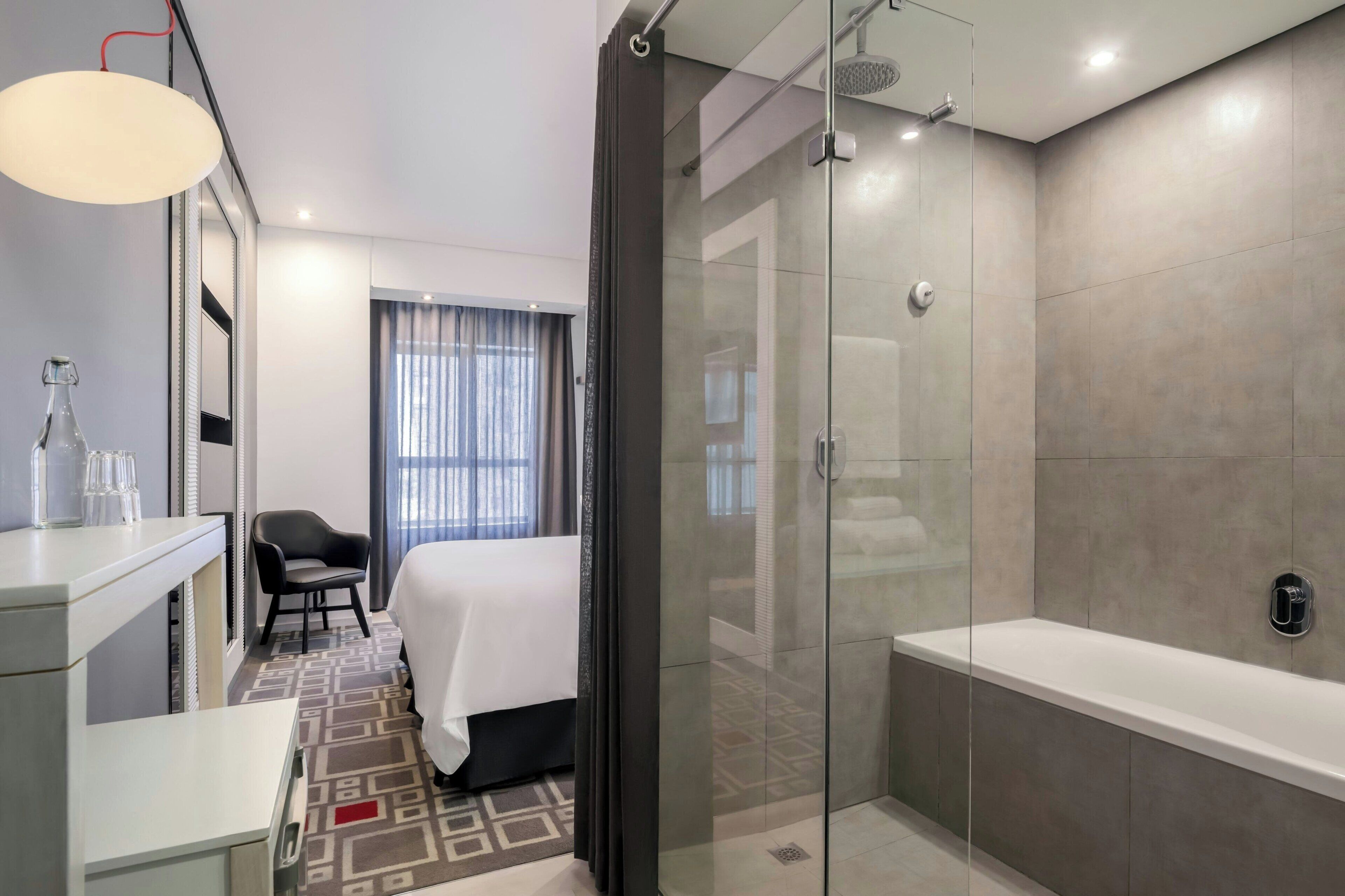 Une salle de bain d’hôtel moderne avec une douche en verre, une grande baignoire et une table de chevet avec une lampe.