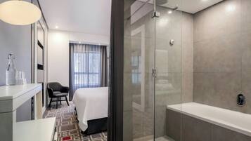 Une salle de bain d’hôtel moderne avec une douche en verre, une grande baignoire et une table de chevet avec une lampe.