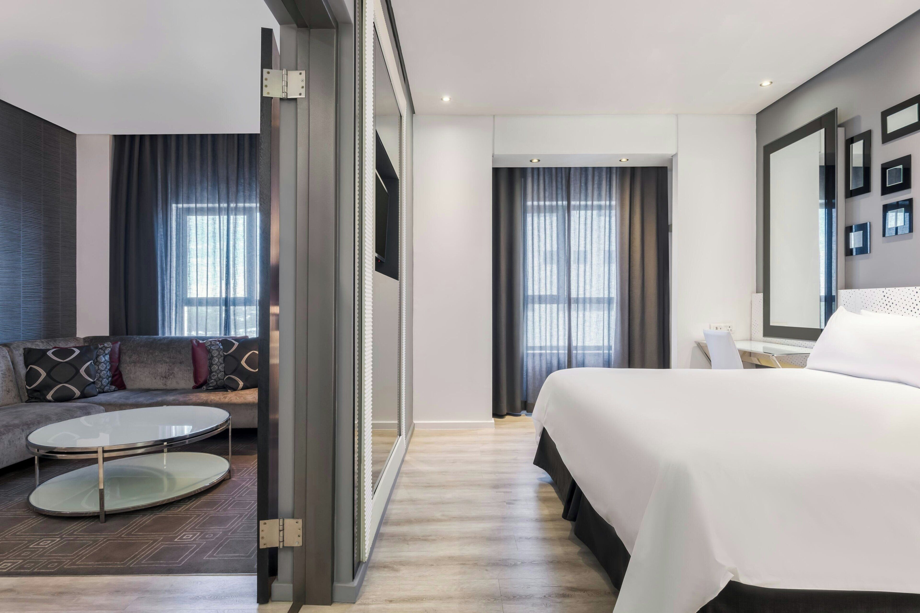 Una habitación de hotel moderna con una cama, un sofá, una mesita redonda y un espejo grande.