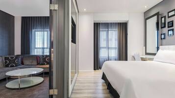 Una habitación de hotel moderna con una cama, un sofá, una mesita redonda y un espejo grande.