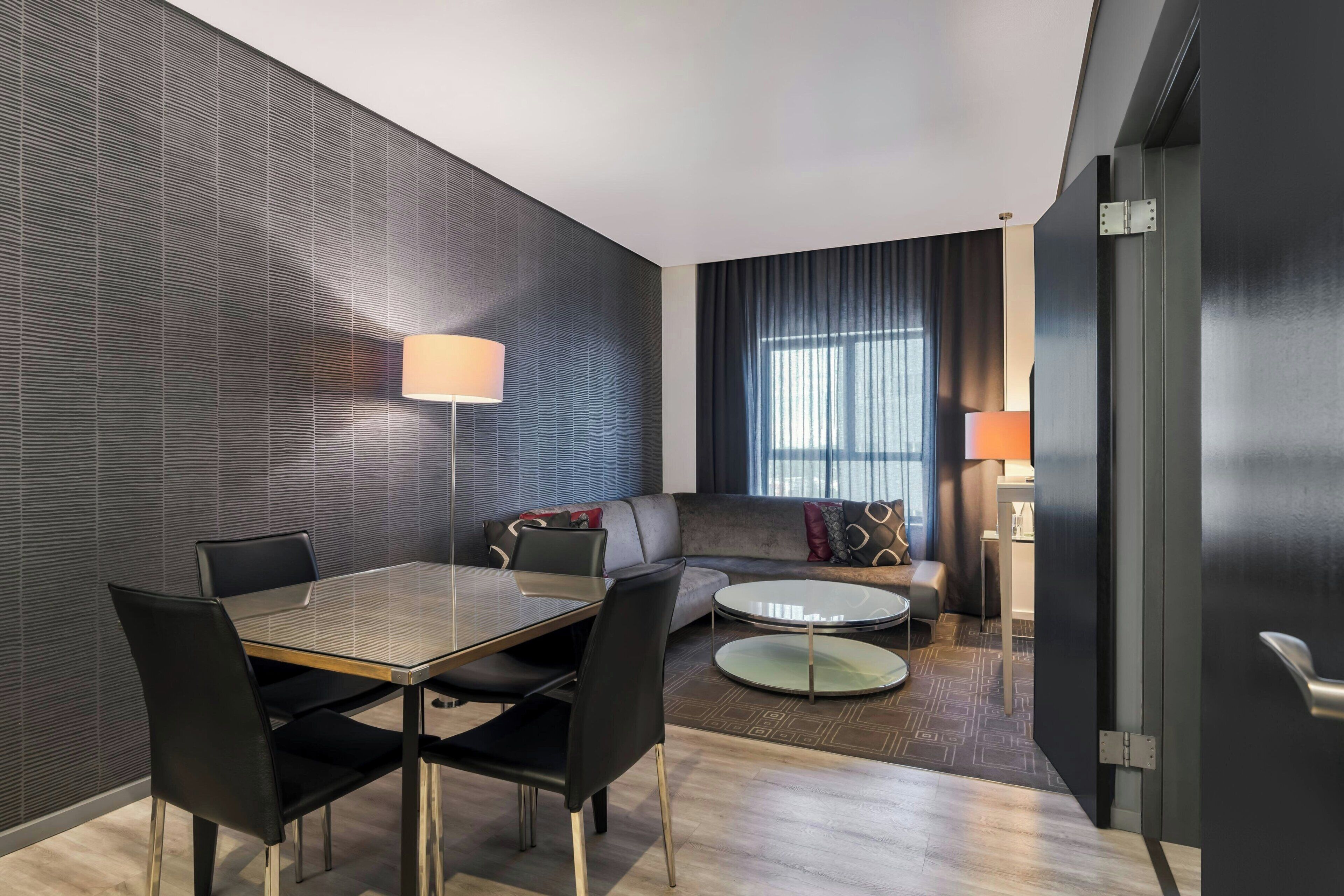 Una habitación de hotel moderna con una mesa de comedor, sillas, un sofá y una mesa redonda de centro.