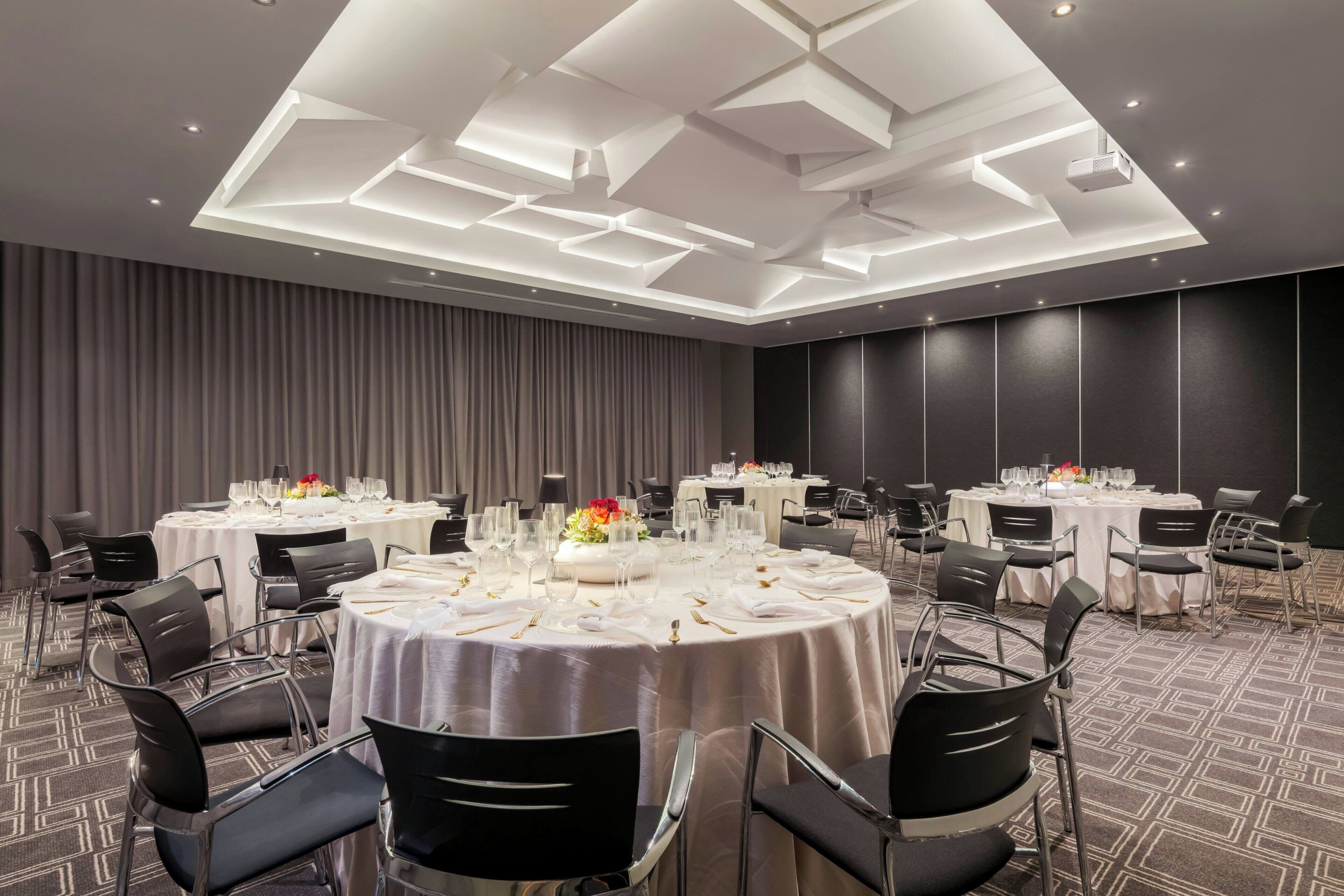 A conference room with round tables, black chairs, and a modern ceiling design.