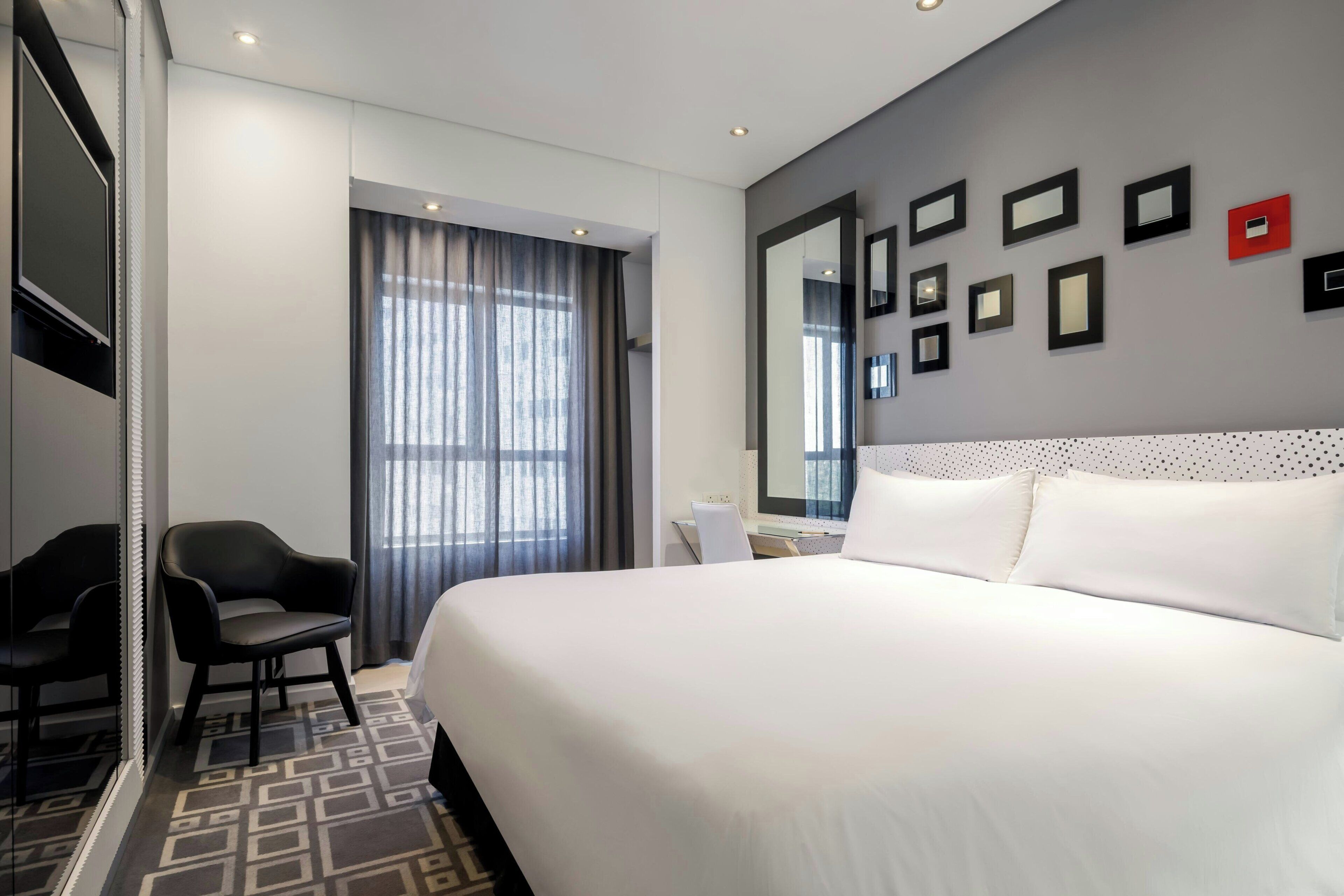 Habitación de hotel con una cama grande, un escritorio, una silla, un televisor y una ventana con cortinas.