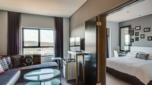 A modern hotel room with a large bed, a sofa, a small desk, and a view of the city. - Protea Hotel Fire & Ice by Marriott Pretoria Menlyn (Pretoria)
