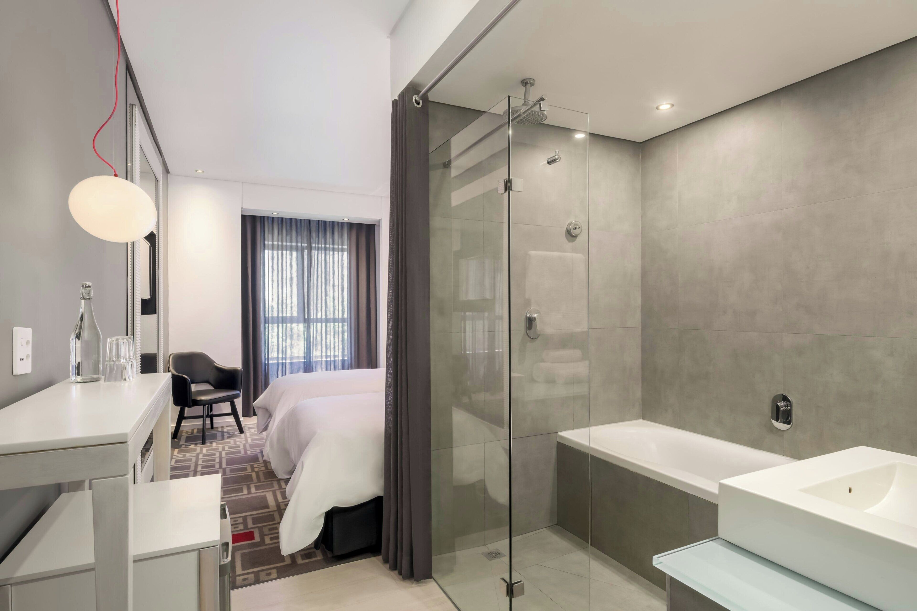 A modern hotel bathroom with a glass-enclosed shower, a large bathtub, and a separate sink area.