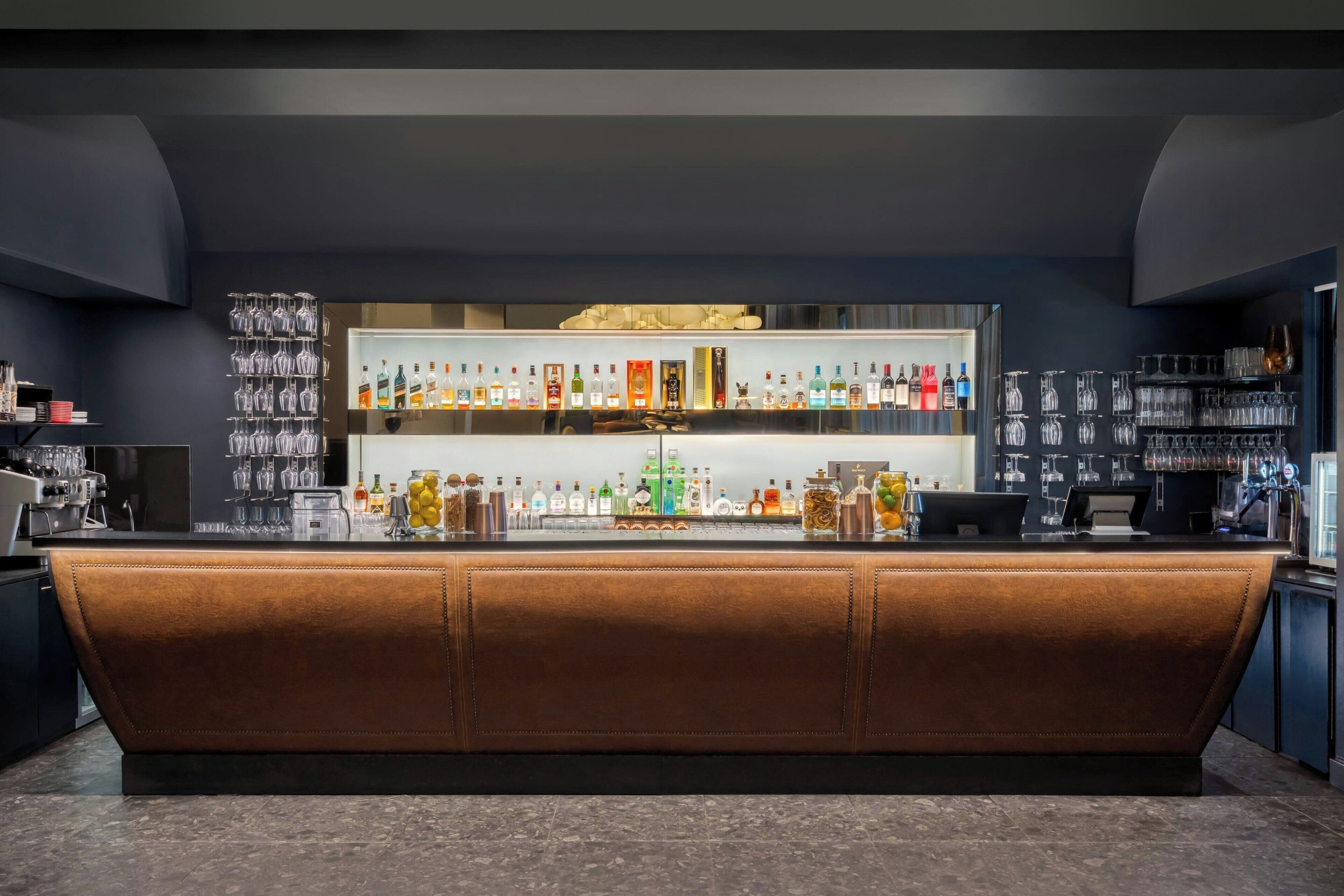 Un bar avec un comptoir en cuir, des étagères remplies de bouteilles et des verres.