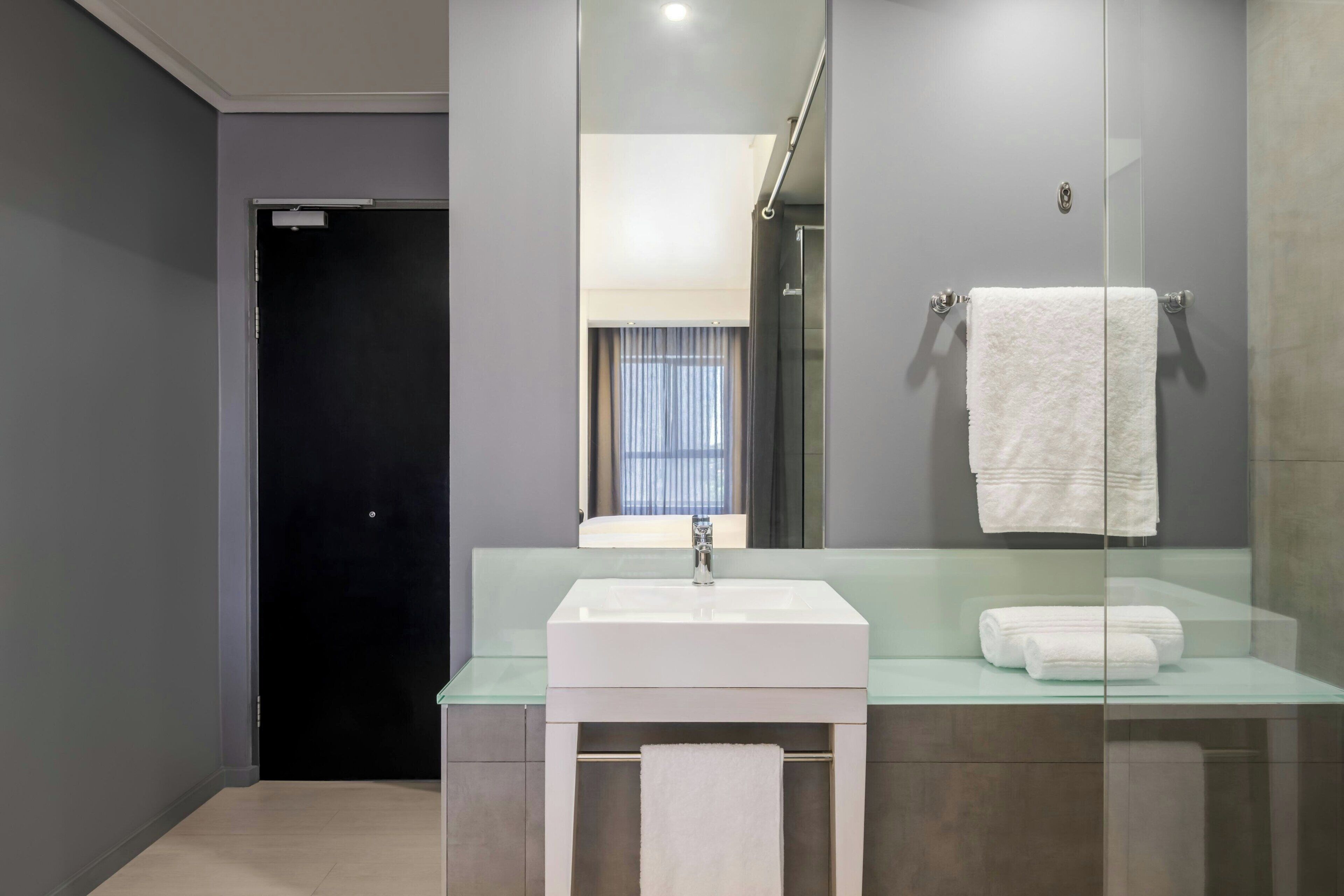 Een moderne badkamer met een glazen wastafel, een spiegel en een handdoekrek.