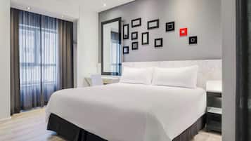 A modern hotel room with a large bed, a desk, a mirror, and a wall with framed pictures.