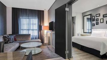 Una habitación de hotel moderna con sofá, una mesa redonda de comedor, cama, televisor y escritorio con lámpara.