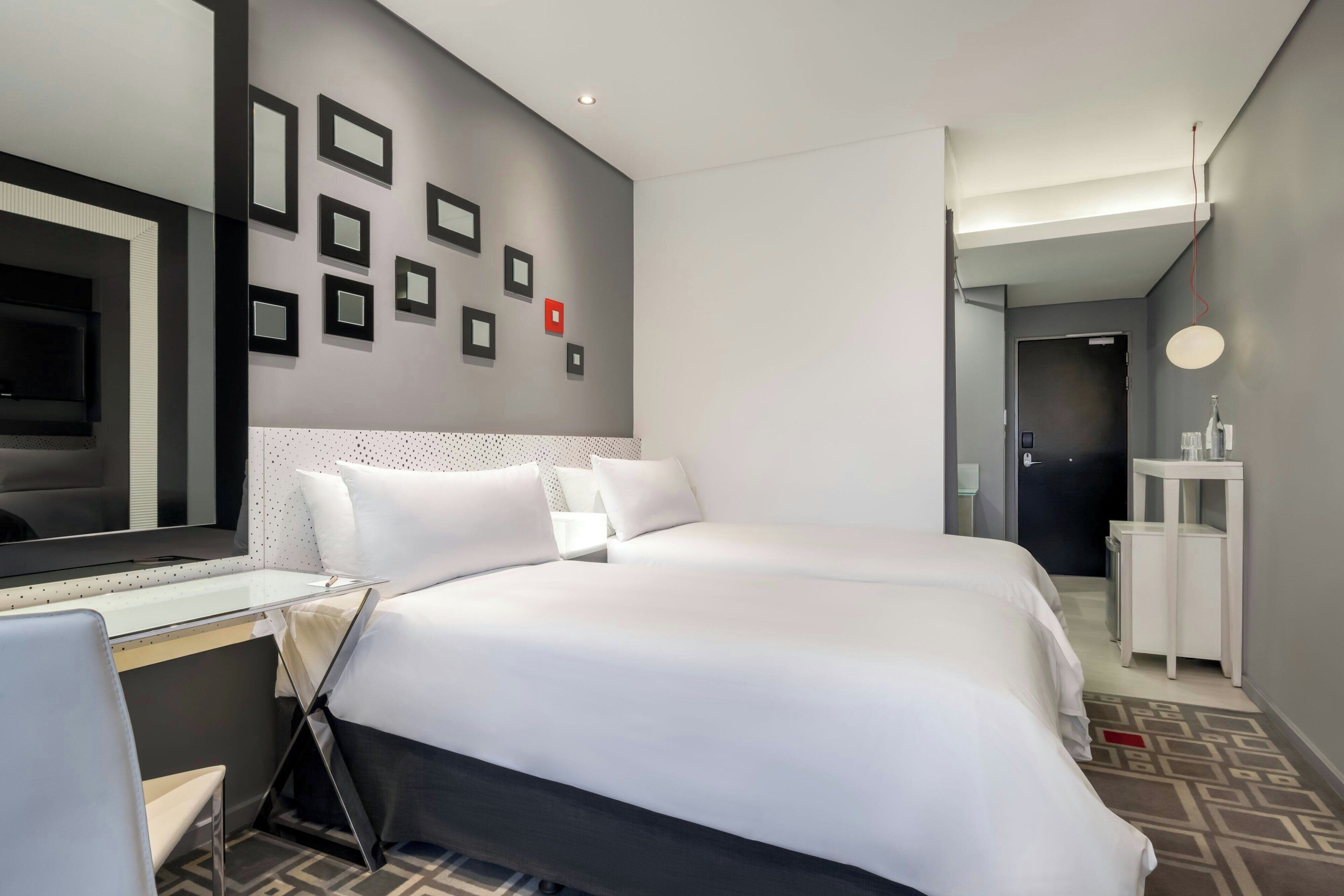 Una habitación de hotel con una cama grande, un escritorio, una silla, un espejo y una pared con cuadros.