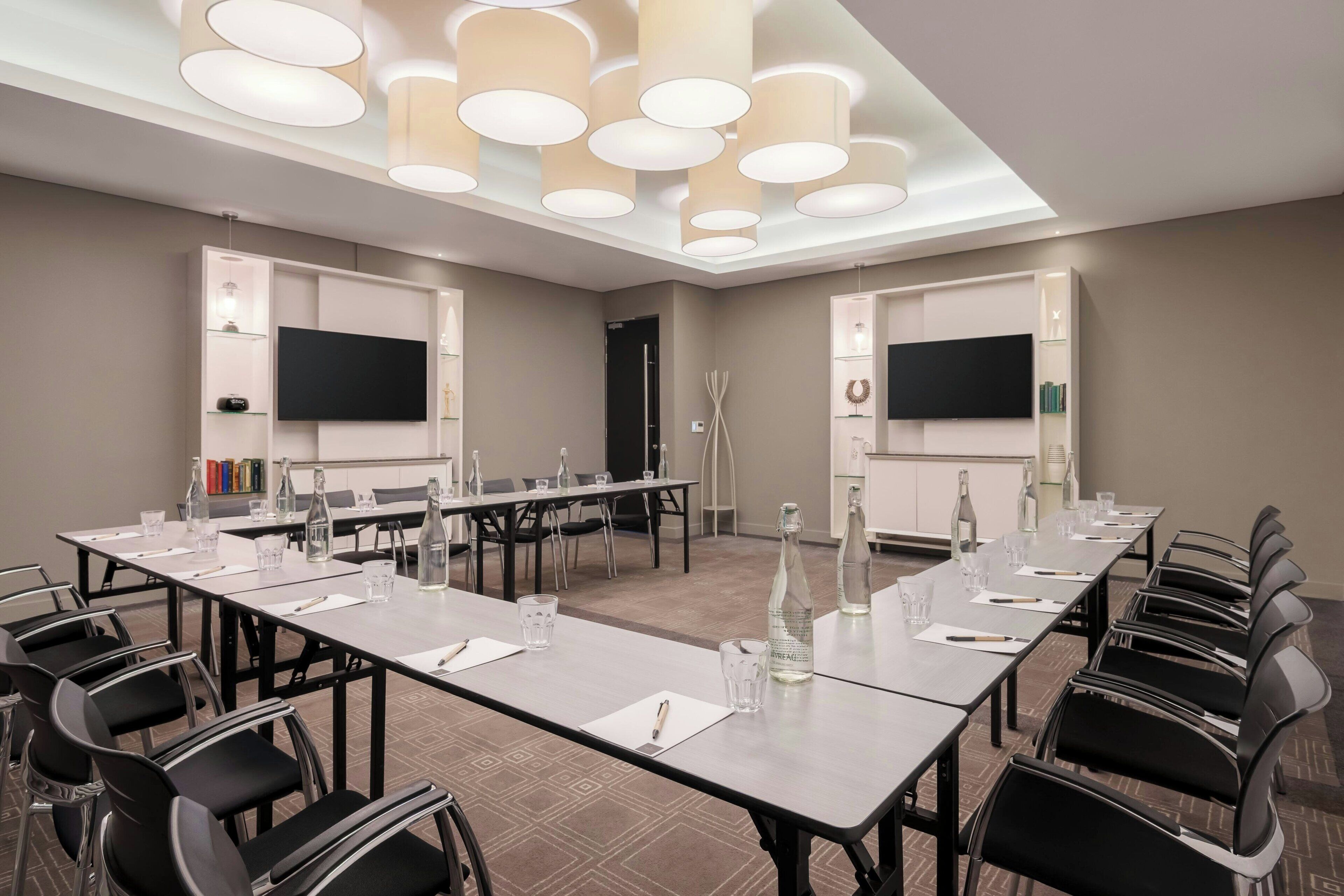 A conference room with a long table, chairs, a flat-screen TV, and a ceiling light fixture.