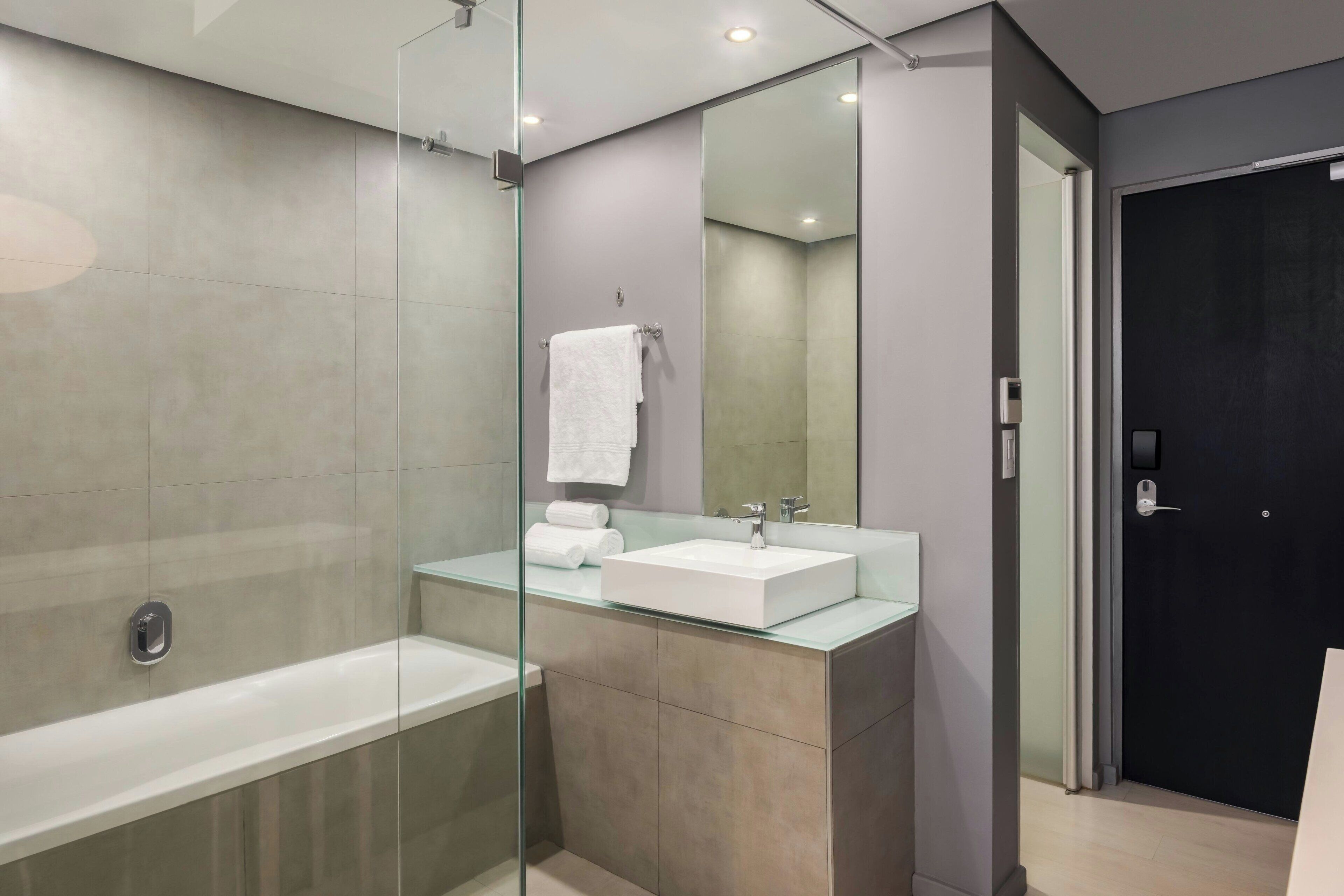 Un baño moderno con ducha de vidrio, un lavamanos blanco y una puerta oscura.