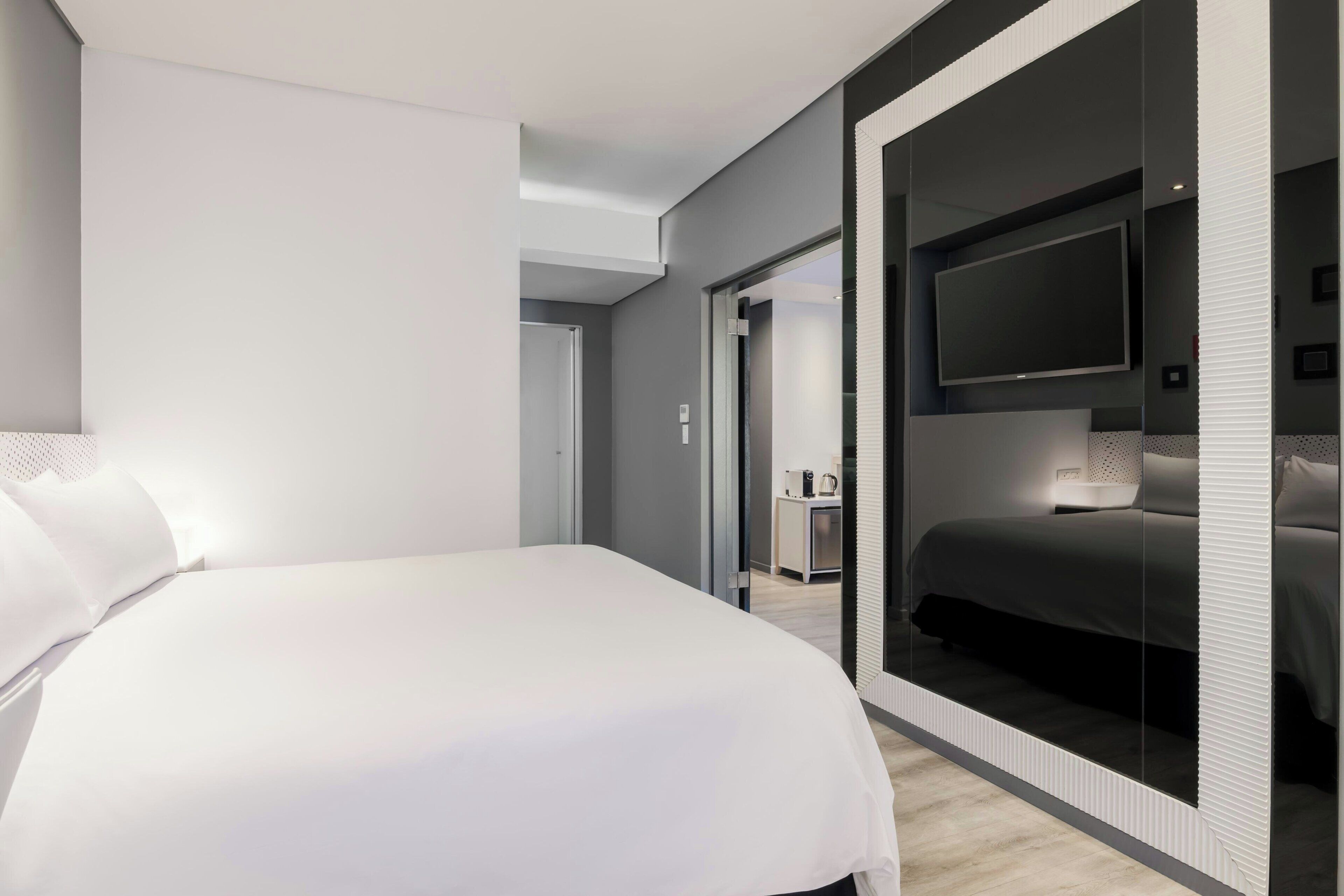 Una habitación de hotel moderna con una cama grande, un televisor y un espejo.