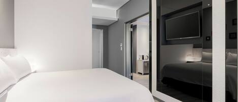 A modern hotel room with a large bed, a television, and a mirror.