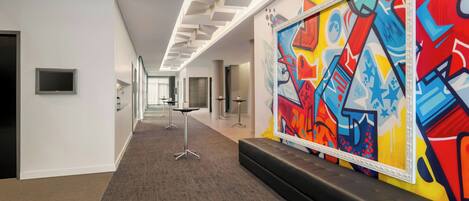 A hallway with a carpeted floor, a black bench, and a colorful abstract painting on the wall.