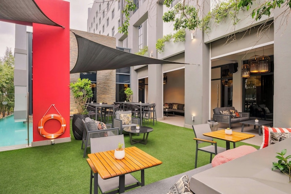 An outdoor patio with tables and chairs, a pool, and a red wall.