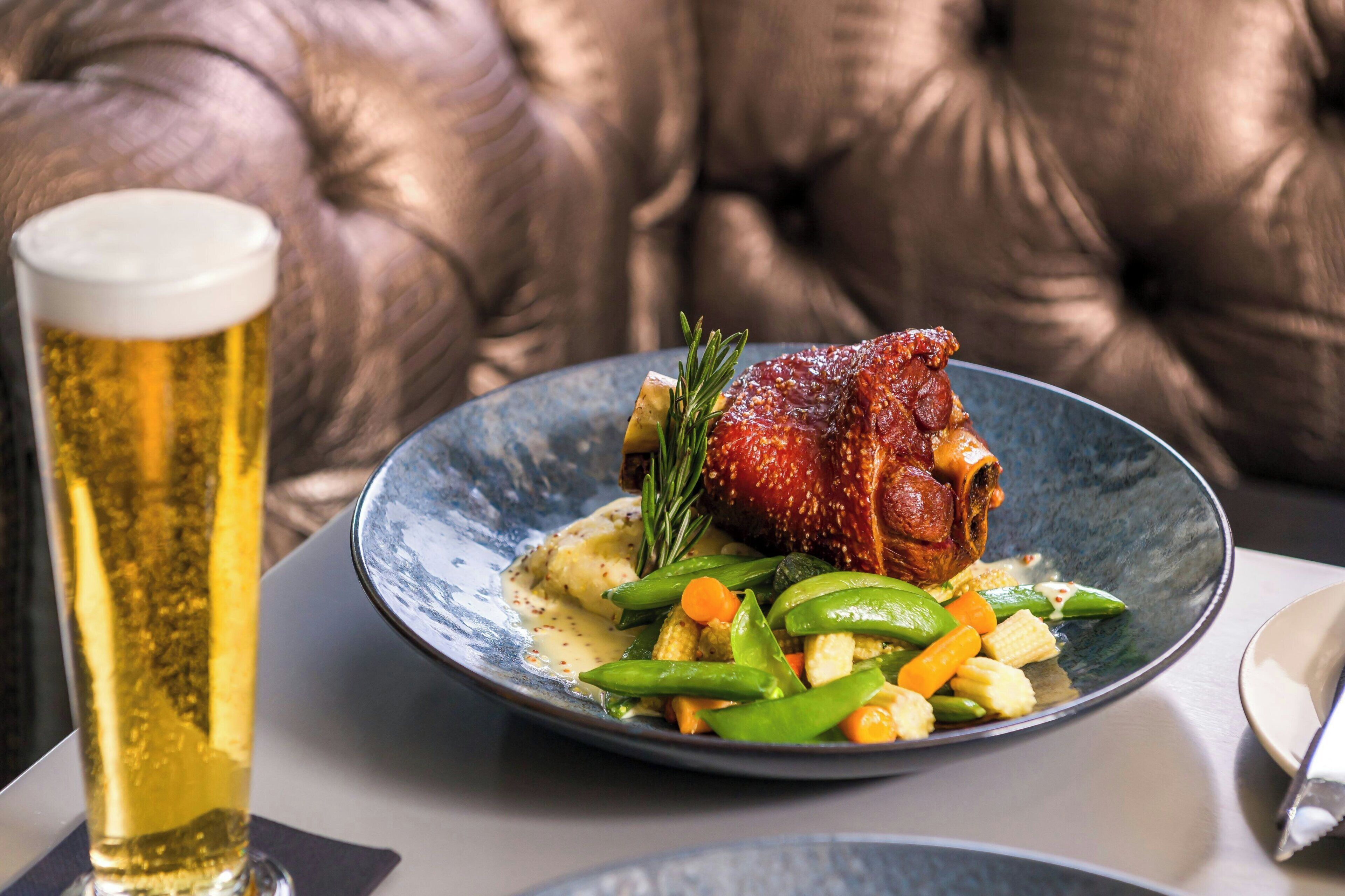 Ein Teller mit Essen, darunter ein Braten, Gemüse und ein Bierglas.