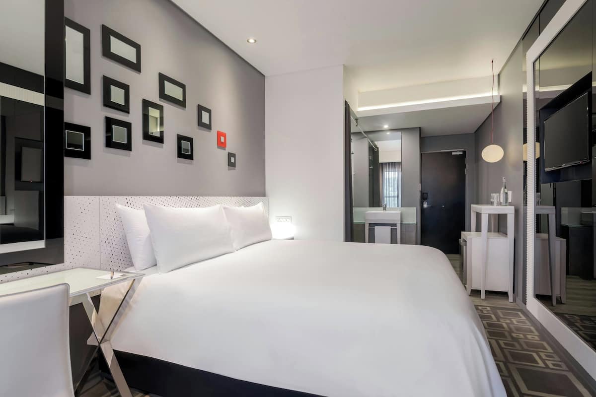 A modern hotel room with a large bed, a desk, a mirror, and a TV.