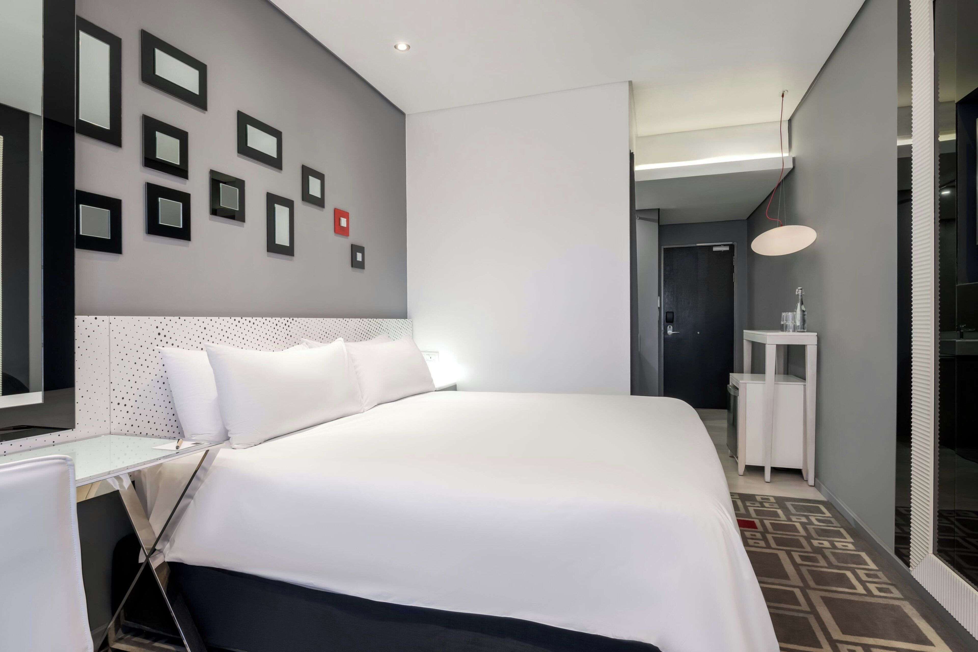 Een moderne hotelkamer met een net opgemaakt bed, een aan de muur bevestigd fotolijstje, een nachtkastje en een klein witte nachtkastje.