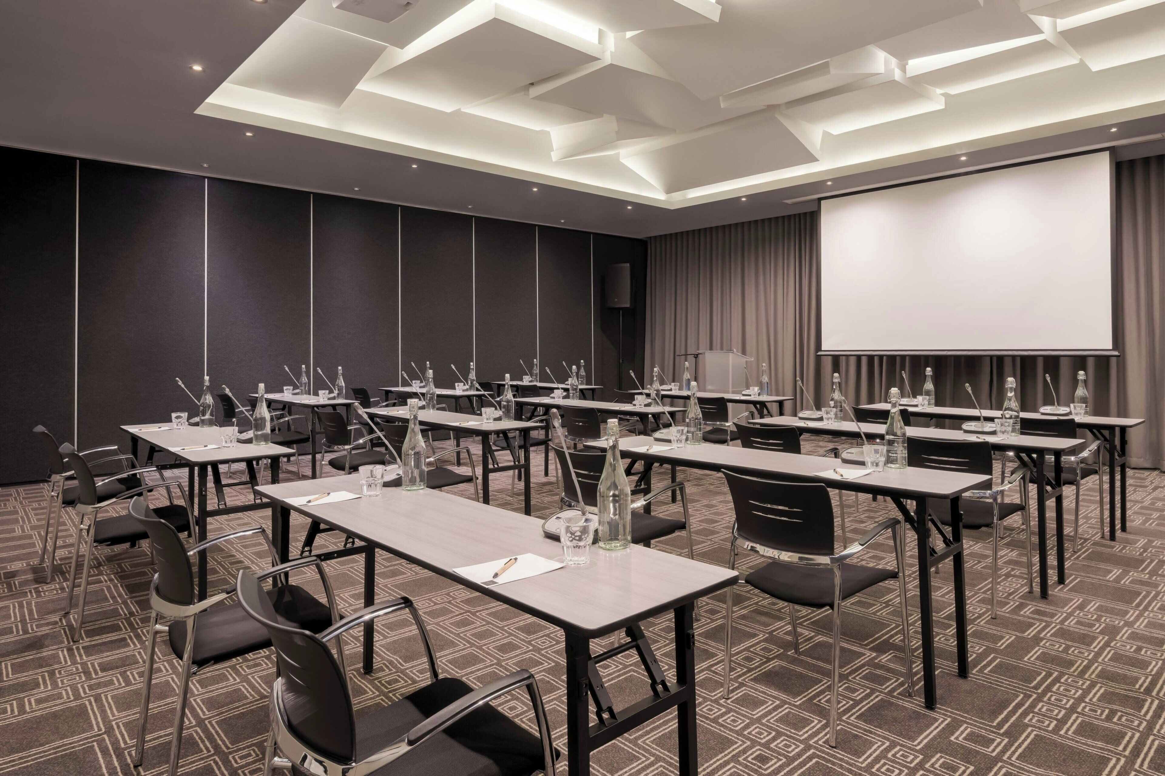 A conference room with tables, chairs, a projector screen, and a speaker.