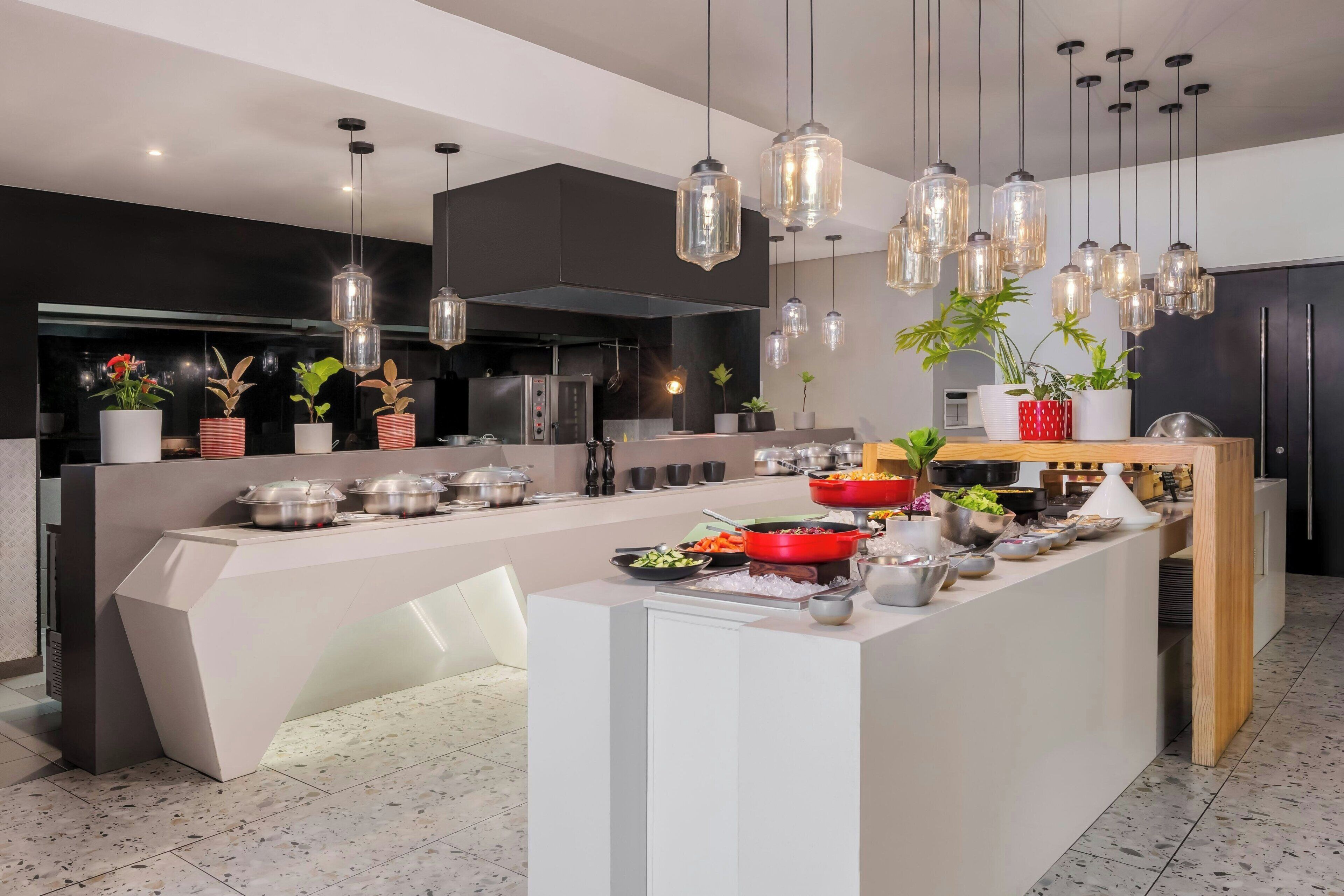 Cocina moderna con una isla central, luces colgantes y plantas en macetas.