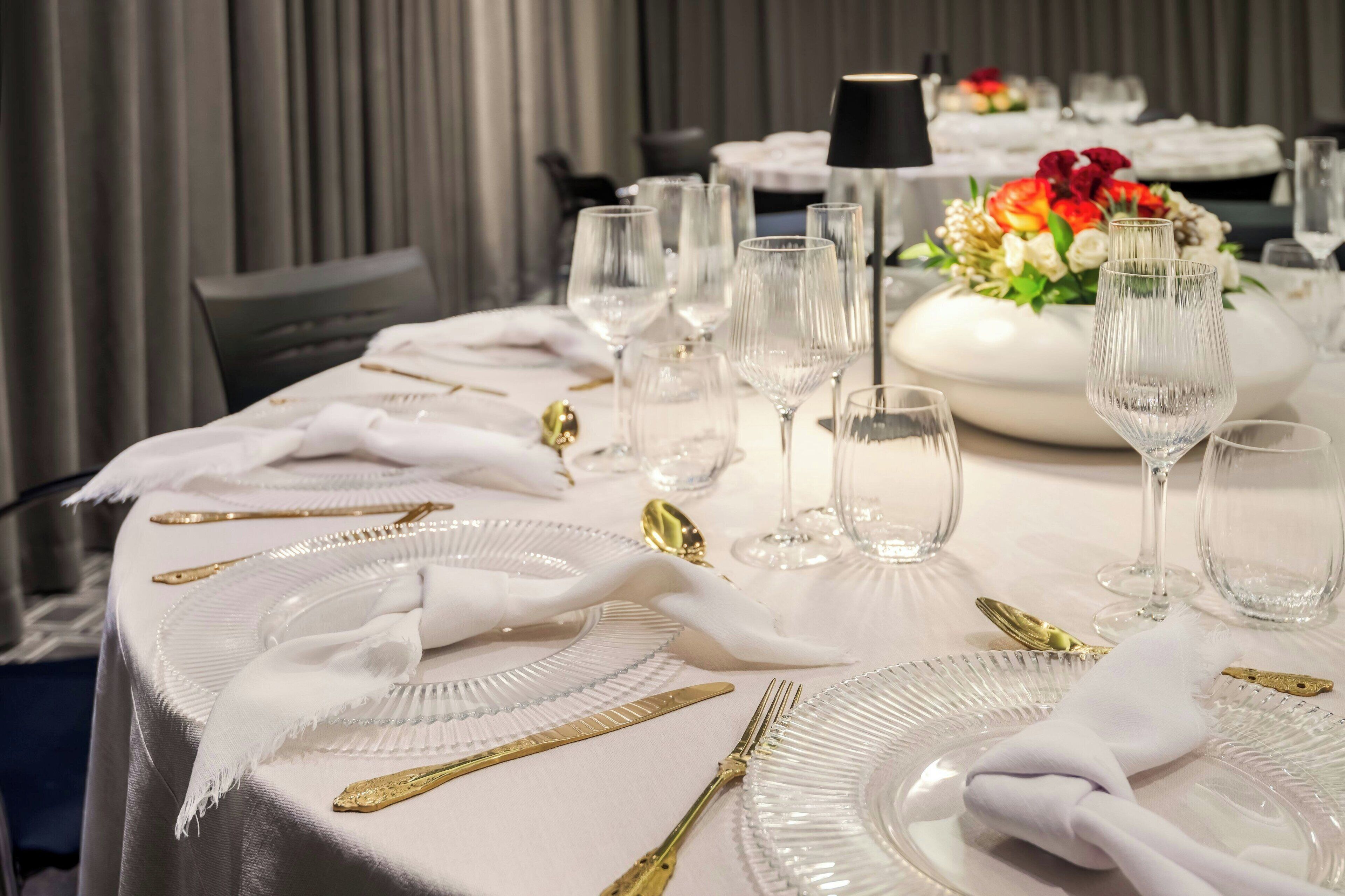 Una mesa vestida con manteles blancos, cubiertos dorados y copas de cristal.