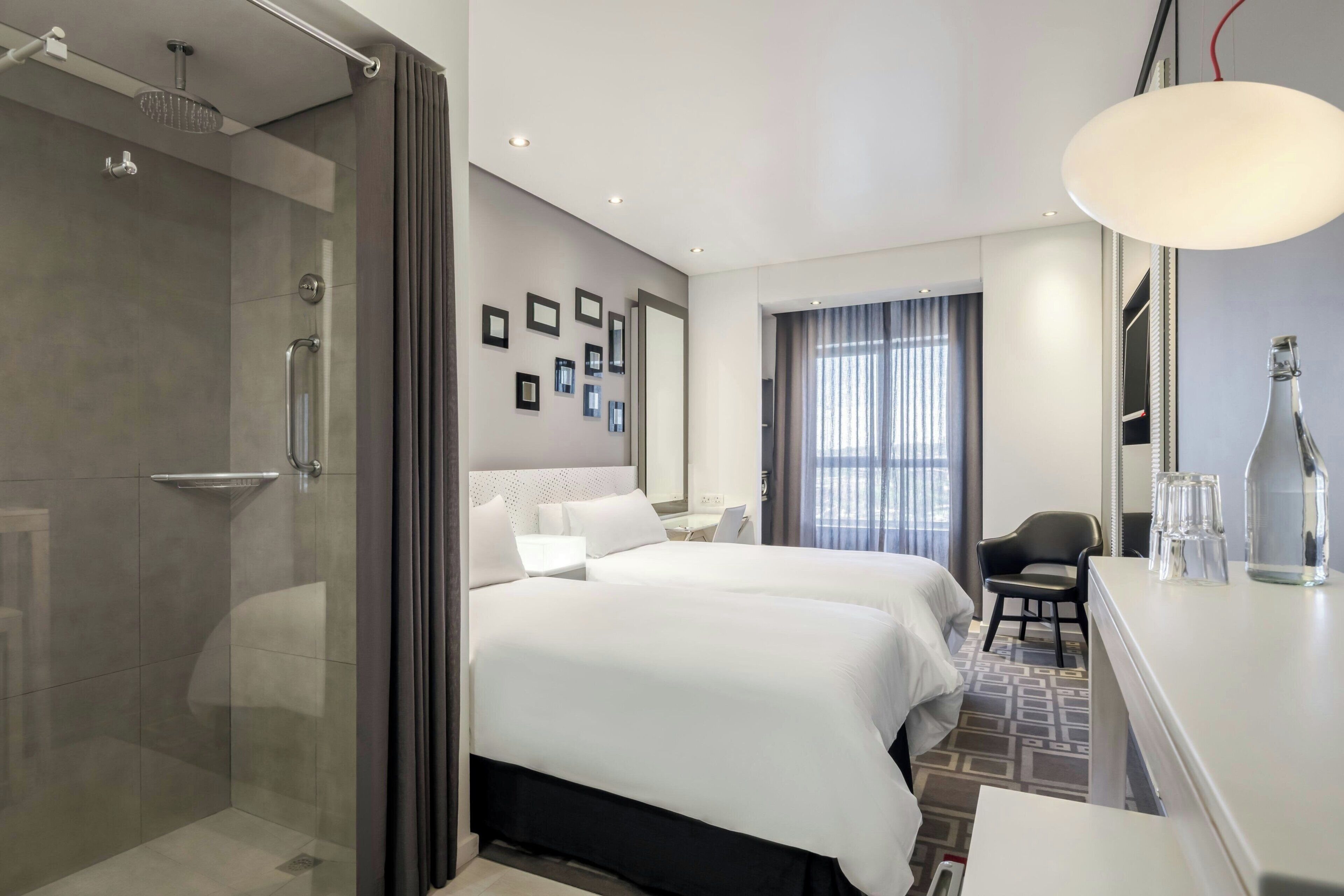 A modern hotel room with a shower, a bed, a desk, and a chair.