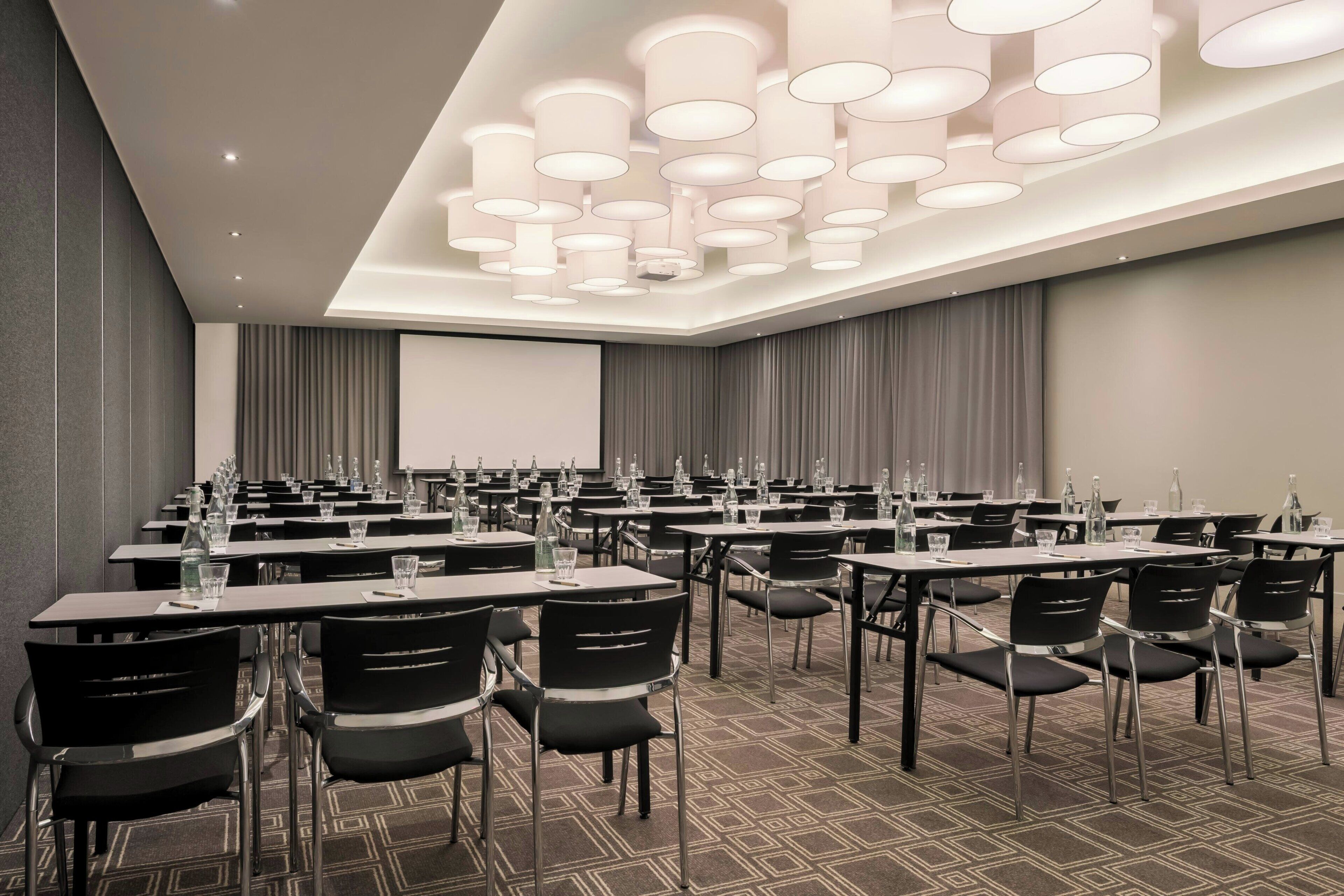 A conference room with tables, chairs, and a projector screen.