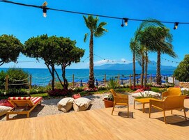 Un área de estar al aire libre con piso de madera, sillones reclinables y vistas al mar.