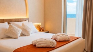Una habitación de hotel con cama, mesita de noche, ventana con cortinas y vista a la playa.
