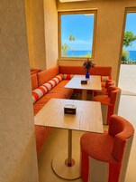 A seating area with a view of the sea, featuring orange and white striped cushions, a small table with a vase, and a wooden floor.