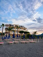 A hotel with multiple floors, outdoor seating with umbrellas, and a mountainous backdrop.