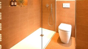 Un baño moderno con ducha de vidrio, inodoro blanco y estante con artículos de aseo.