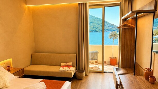 Habitación de hotel con cama, sofá, mesa de madera, planta en maceta y vista al mar.