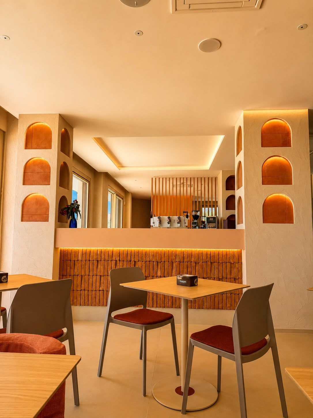 A modern restaurant interior with a central dining area, wooden accents, and a visible kitchen in the background.