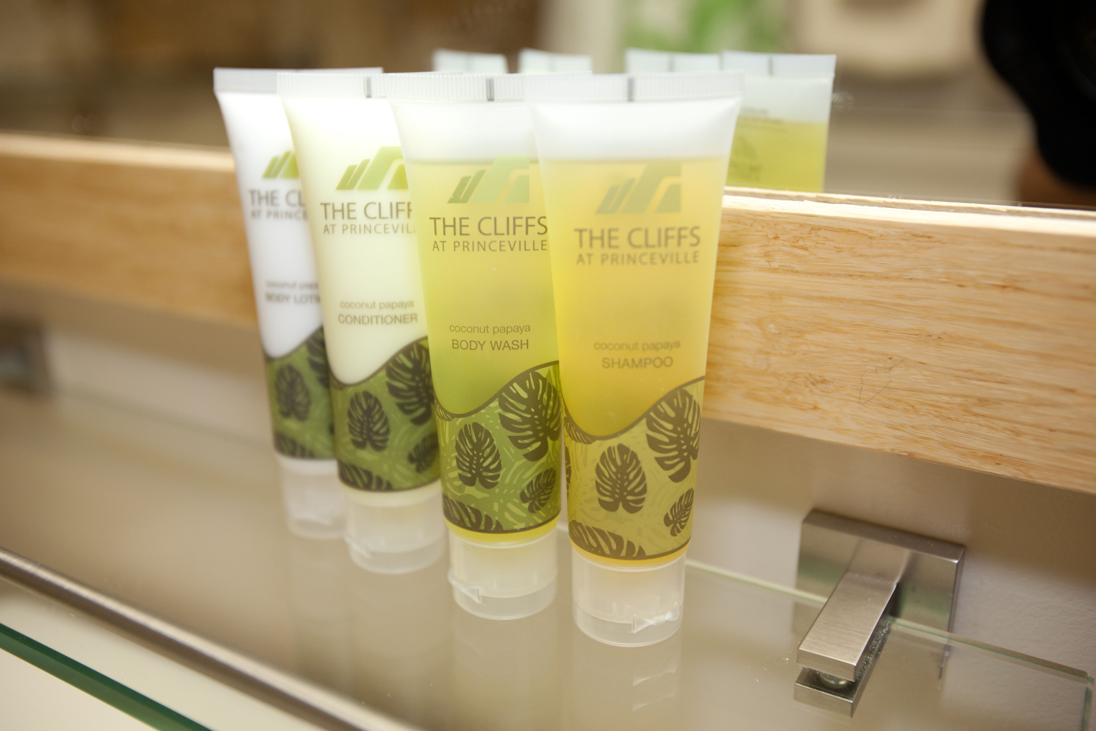 A row of The Cliffs at Princeville body wash and shampoo tubes on a glass shelf.