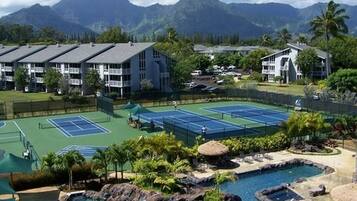 Un complejo turístico con varias canchas de tenis, una piscina con cascada y edificios con balcones.