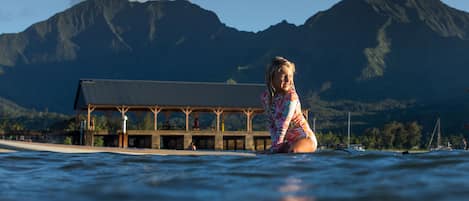 A person in a colorful swimsuit in a body of water with a building and mountains in the background.