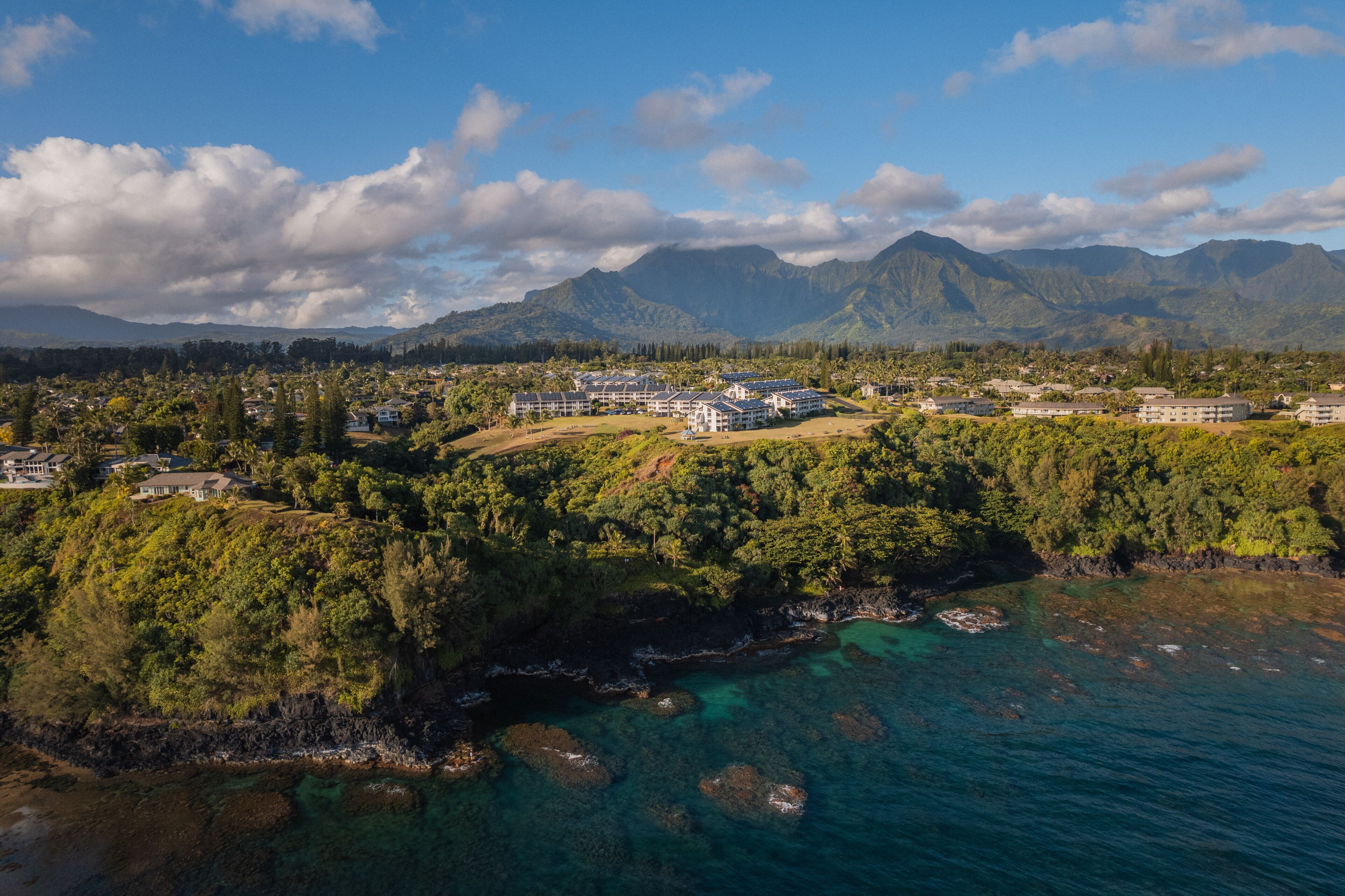 Luftaufnahme eines Küstenresorts mit mehreren Gebäuden, üppiger Vegetation und klarem, türkisblauem Wasser.