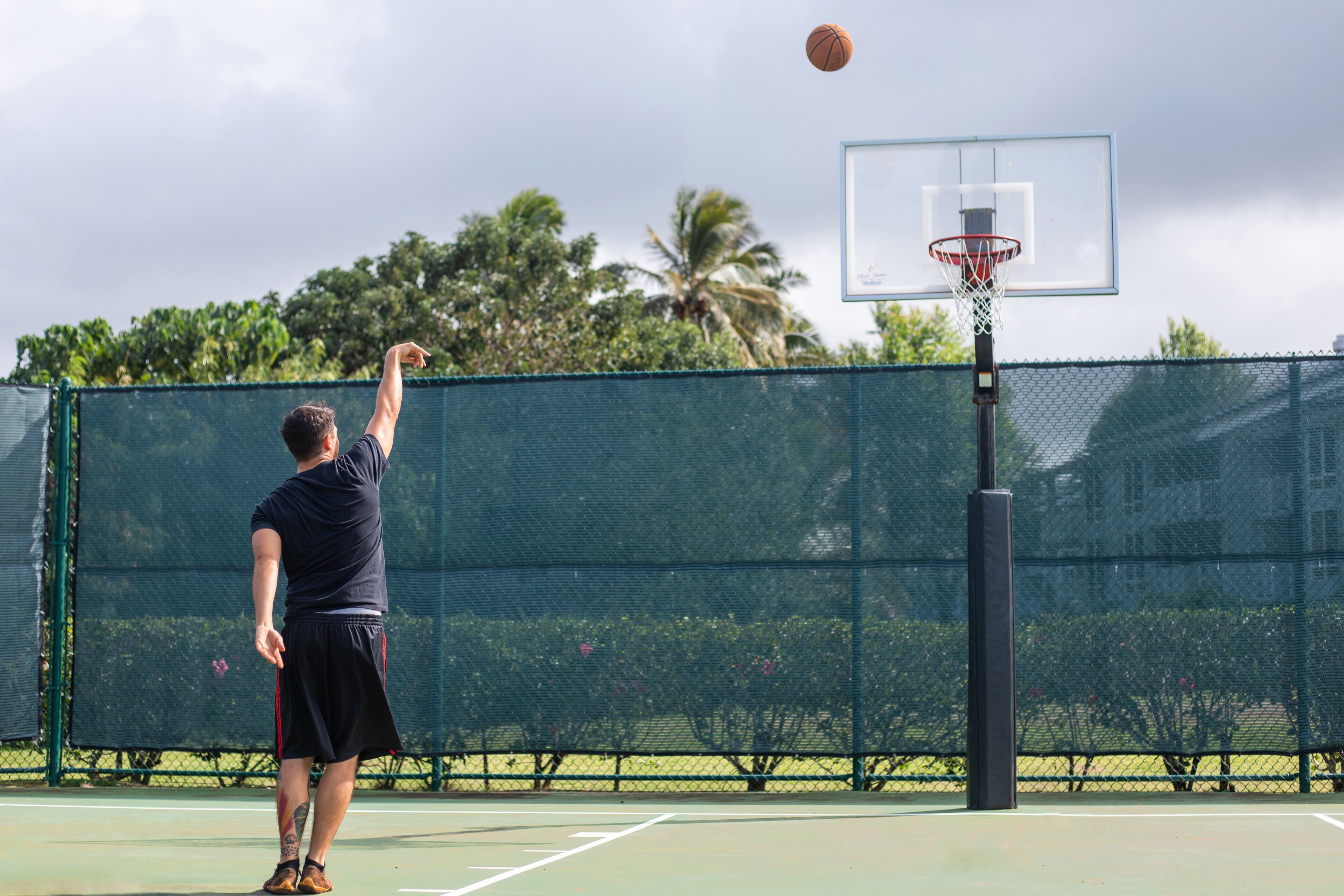 A basketball court with a net, a hoop, and a player in a dark shirt and shorts.
