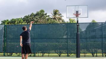 A basketball court with a net, a hoop, and a player in a dark shirt and shorts.