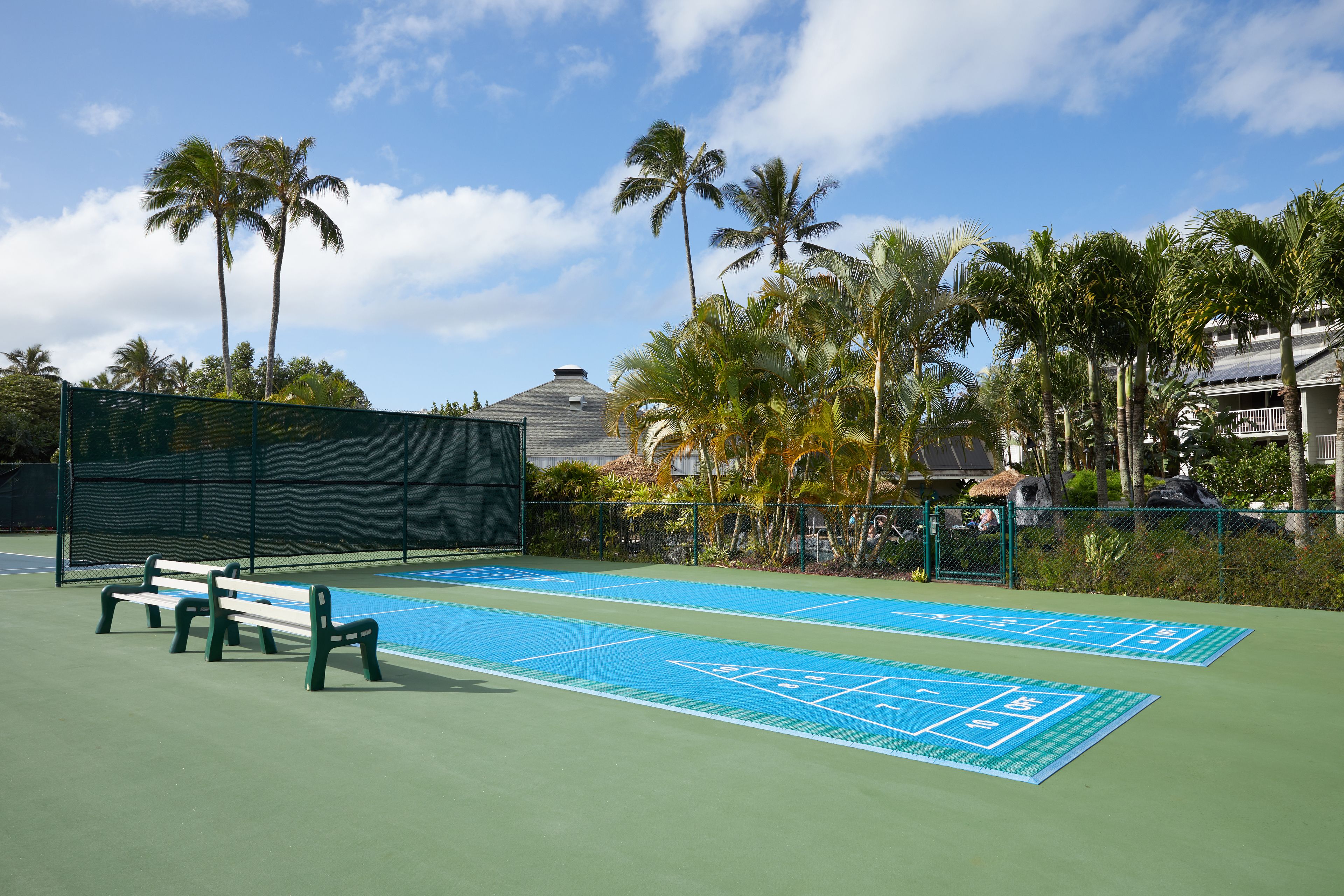 Un court de tennis avec un filet, des bancs et une aire de jeu de palet glissé bleue.