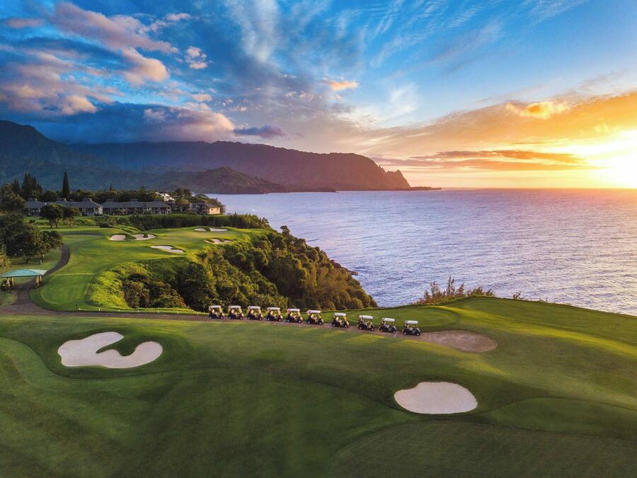A golf course with bunkers and a view of the ocean at sunset.