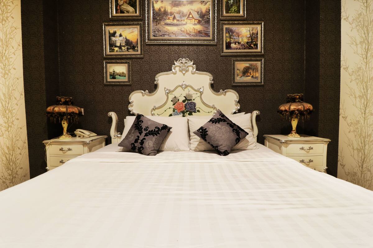 A bedroom with a large bed, ornate headboard, and multiple framed pictures on the wall.