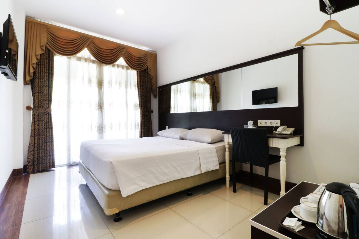 A hotel room with a bed, a desk with a telephone, a mirror, and a hanging coat rack.